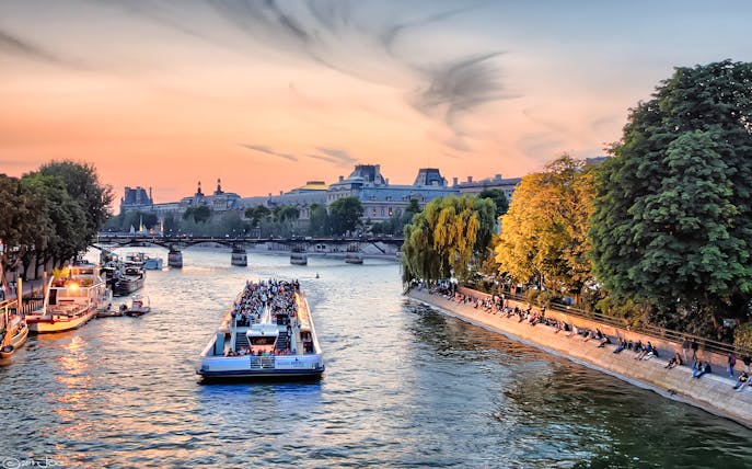 Seine River cruise boat passing under a bridge in Paris at sunset.
