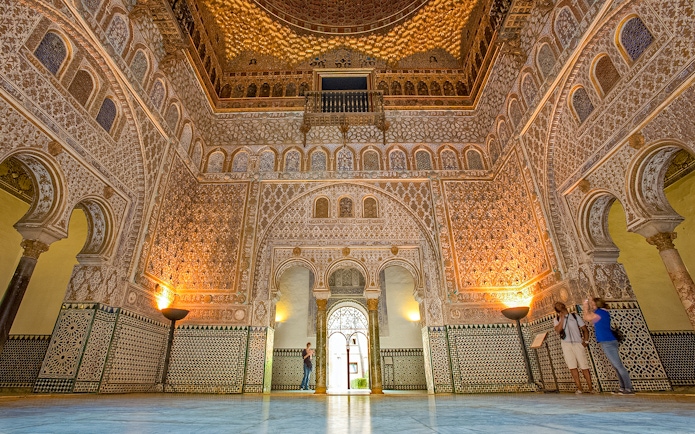 Ornate interior of the Alcazar of Seville with intricate tilework and arches.