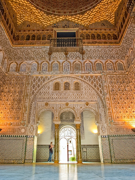 Ornate interior of the Alcazar of Seville with intricate tilework and arches.