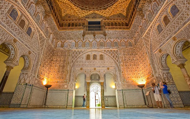 Ornate interior of the Alcazar of Seville with intricate tilework and arches.