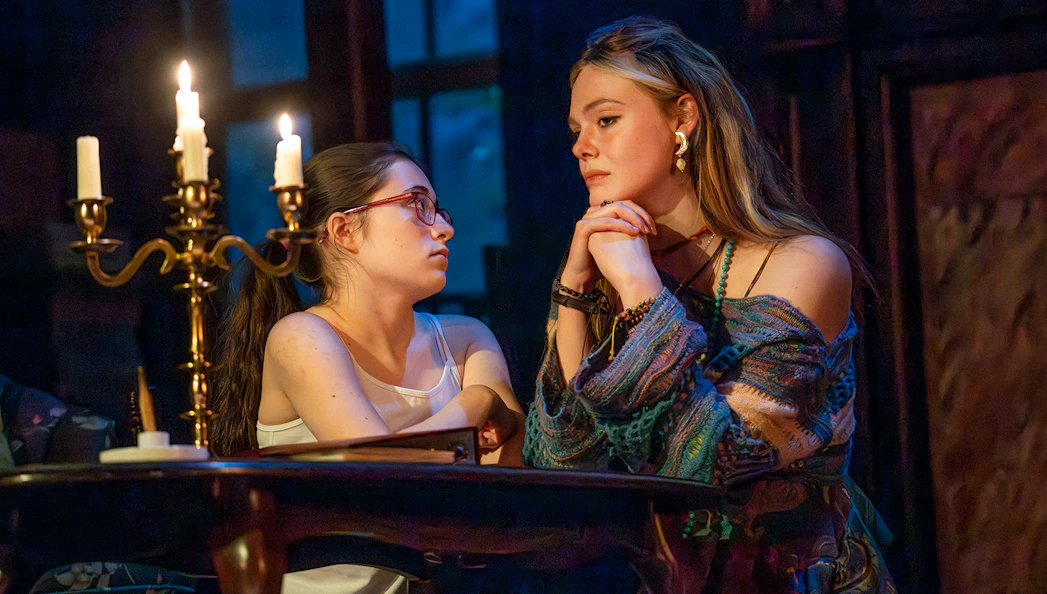Two women sitting at a candlelit table in a dimly lit room, engaged in conversation.
