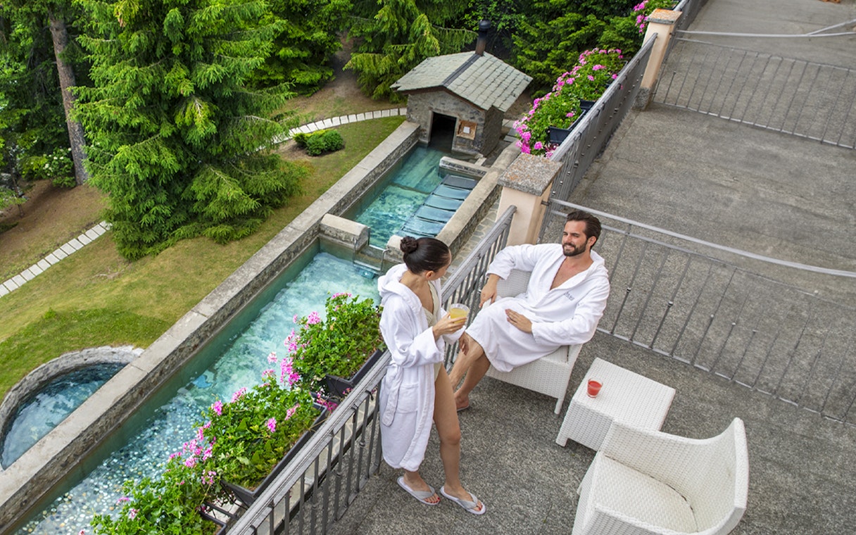 Couple relaxing in robes at QC Terme Bagni Nuovi di Bormio spa terrace.