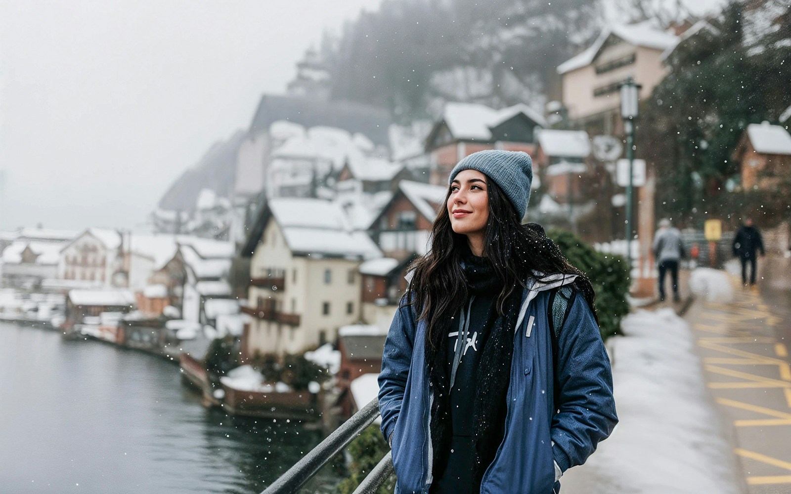 Young woman in winter clothing enjoying snowy Hallstatt, Austria, with traditional houses in the background.