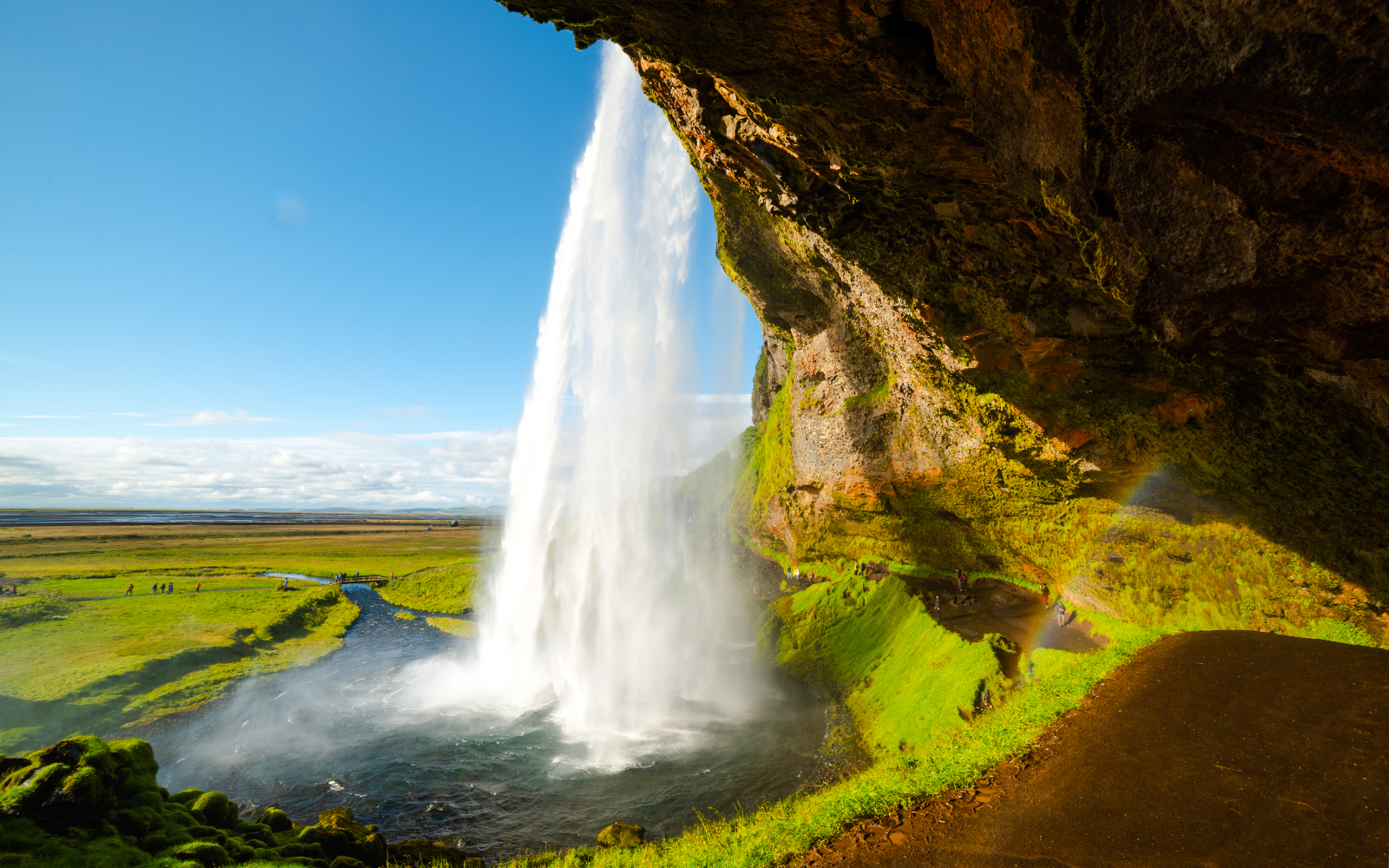 Seljalandsfoss waterfall cascading over a cliff in Iceland with a rainbow in the mist.