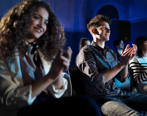 Audience clapping at a theatre show, dressed in casual attire.