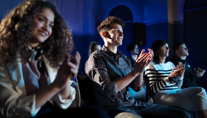 Audience clapping at a theatre show, dressed in casual attire.