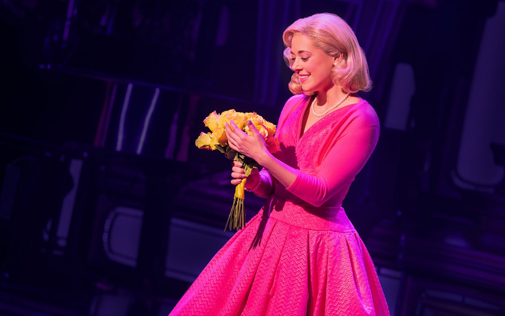 Performer in pink dress holding yellow flowers on stage during "Just In Time" show.