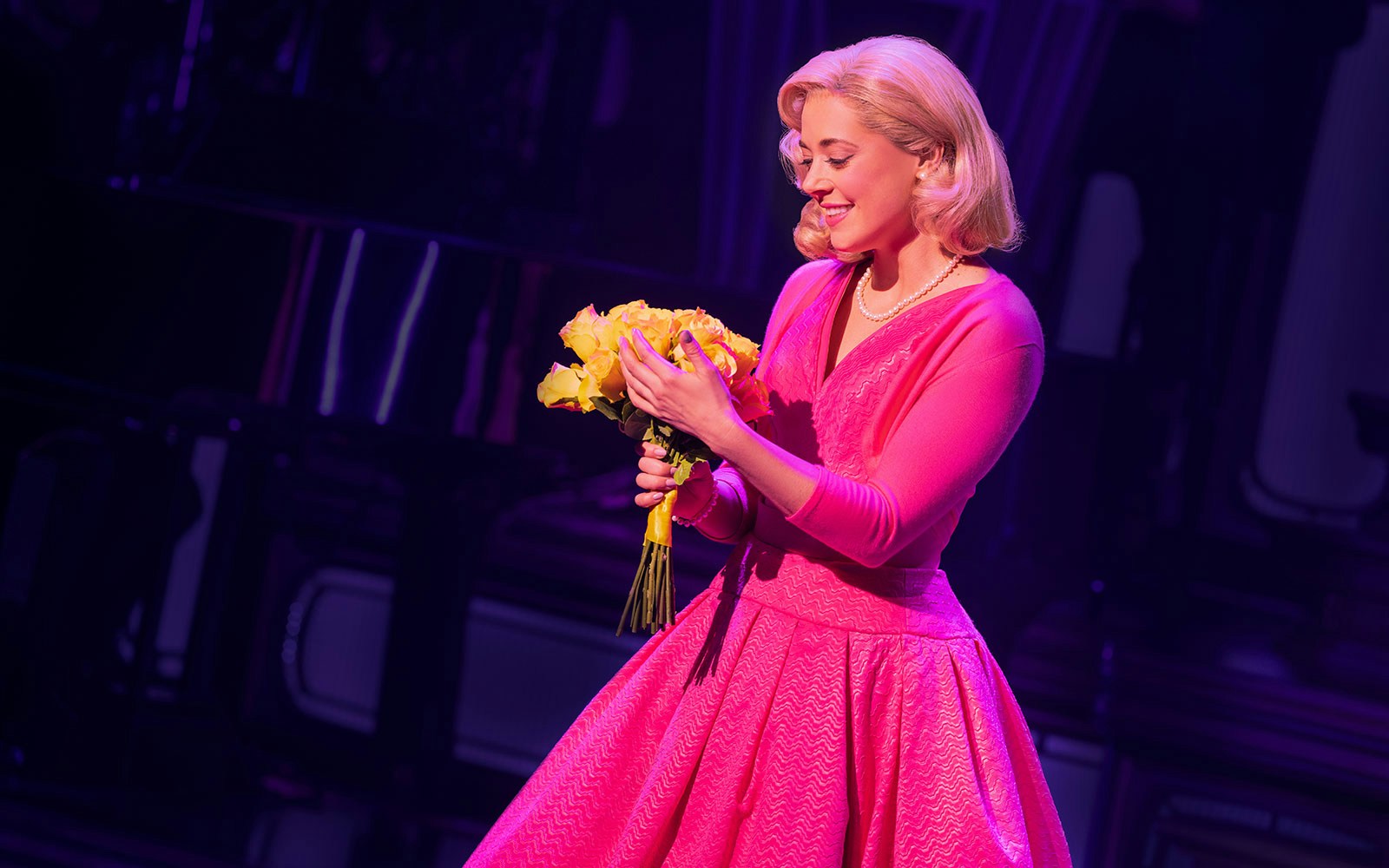 Performer in pink dress holding yellow flowers on stage during "Just In Time" show.