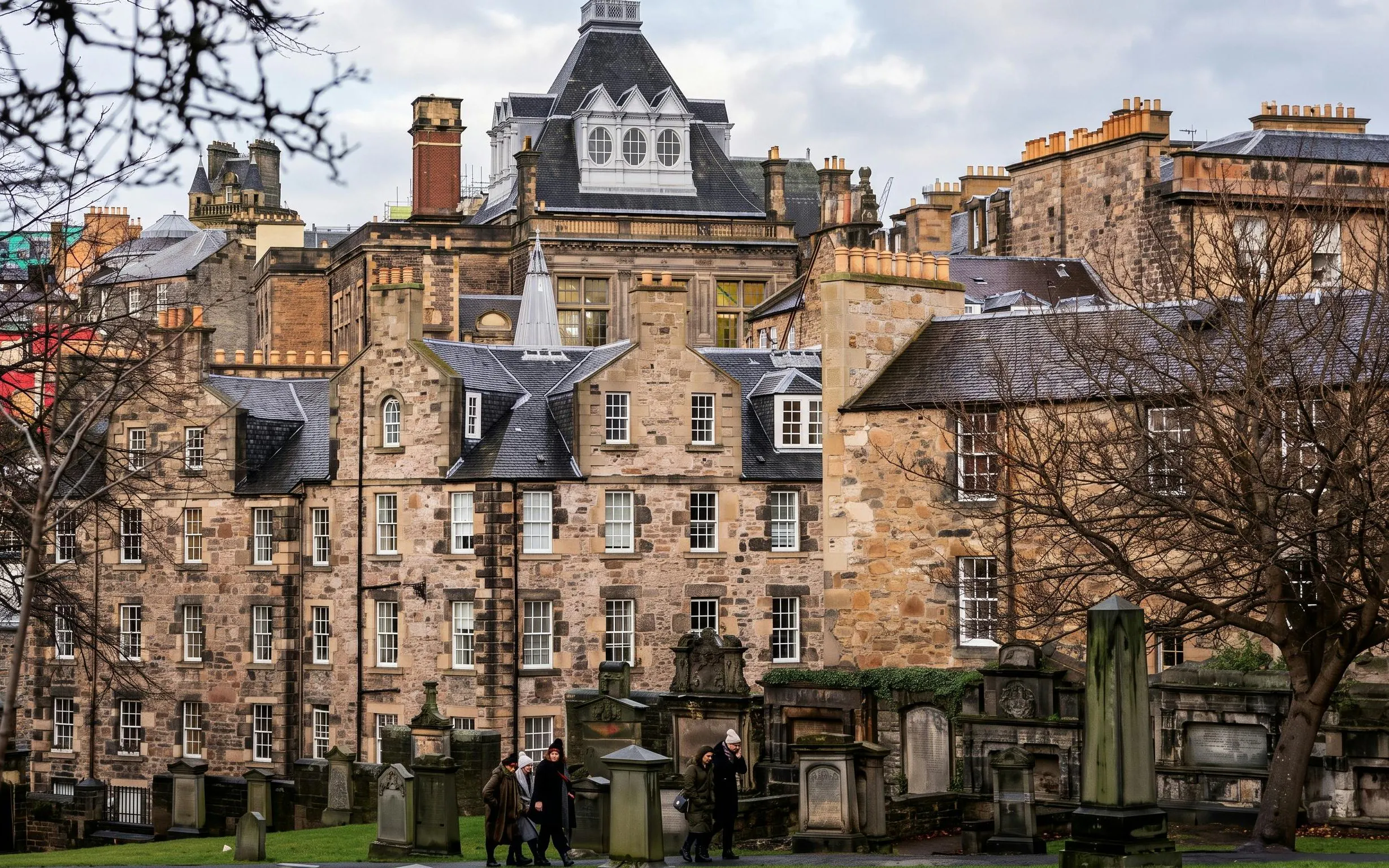 Edinburgh Old Town buildings with tourists walking through a historic graveyard.