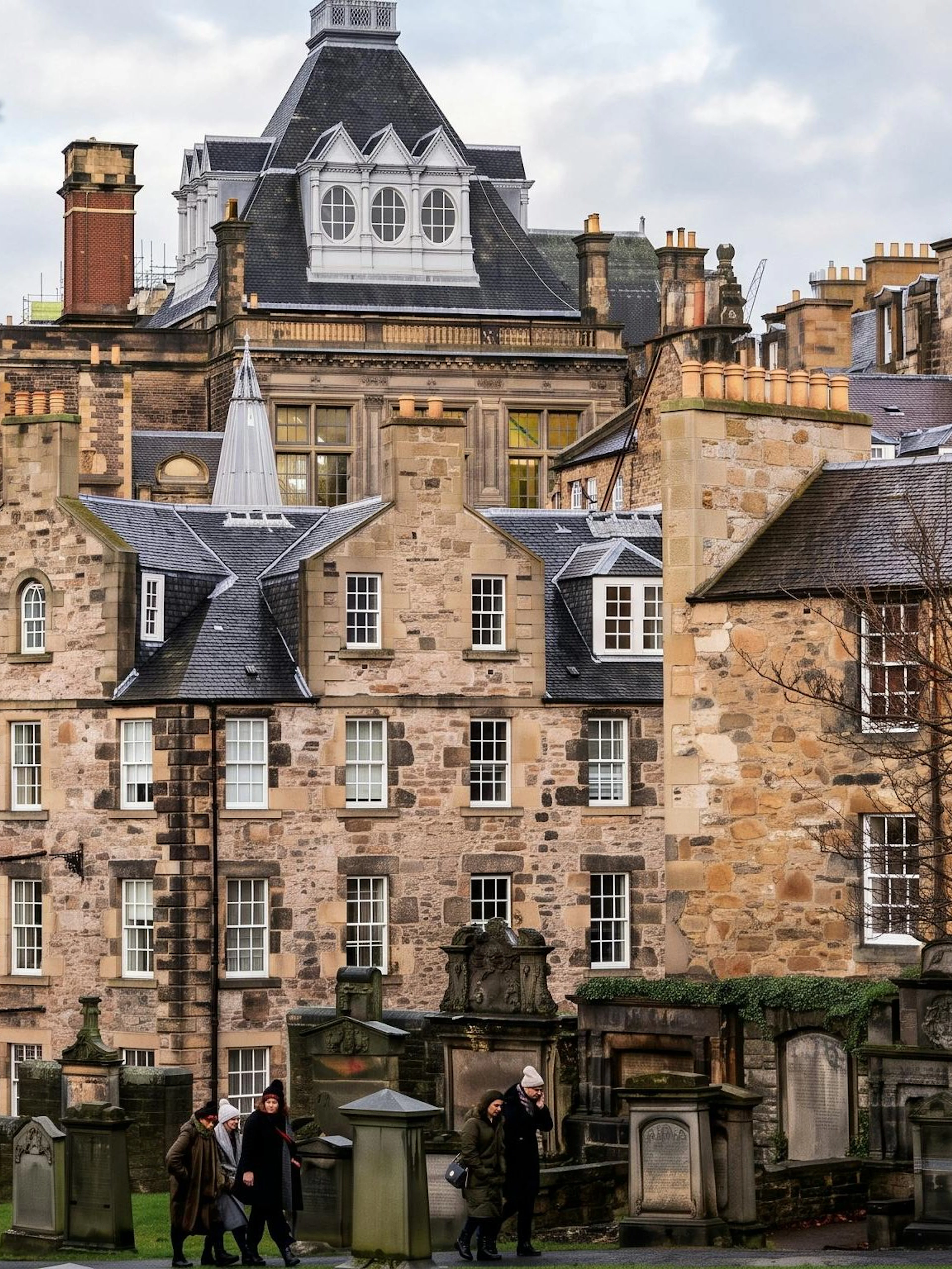Edinburgh Old Town buildings with tourists walking through a historic graveyard.