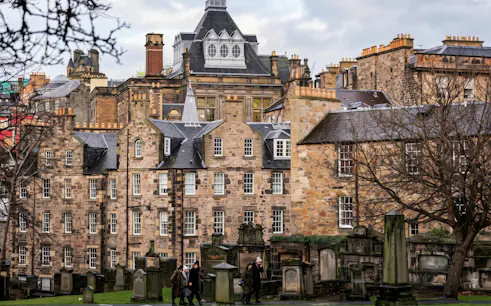 Edinburgh Old Town buildings with tourists walking through a historic graveyard.