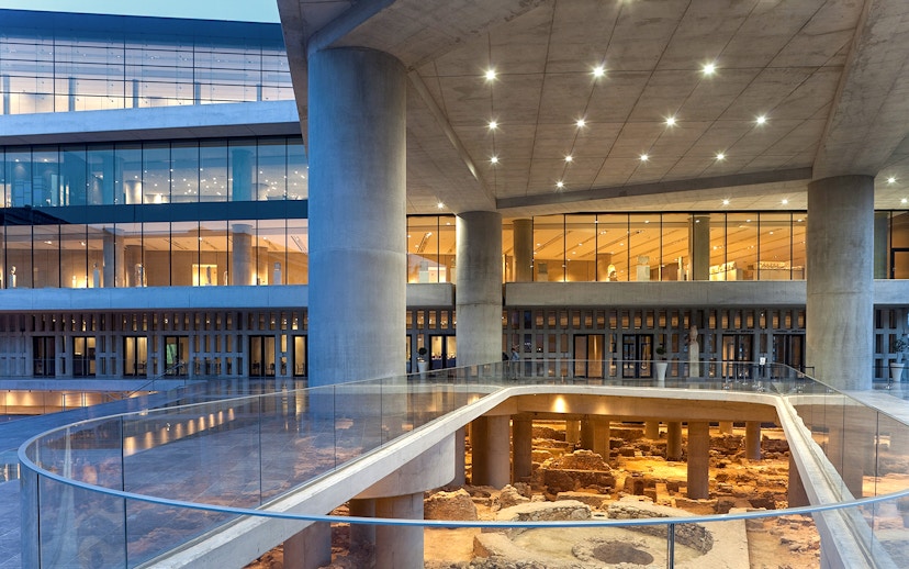 Corridor of Acropolis Museum with glass walkway and ancient ruins below.