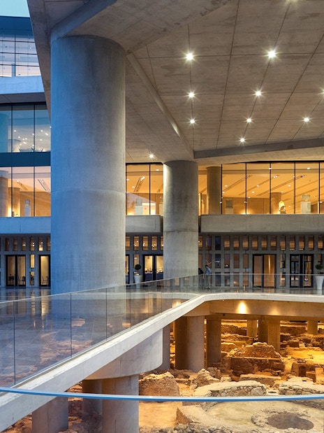 Corridor of Acropolis Museum with glass walkway and ancient ruins below.