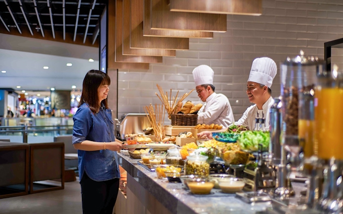 Guest enjoying buffet at Plaza Premium Lounge, KLIA Terminal 2, with chefs preparing food.