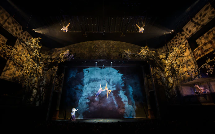 Cirque du Soleil Alizé performers suspended mid-air on a theatrical stage.