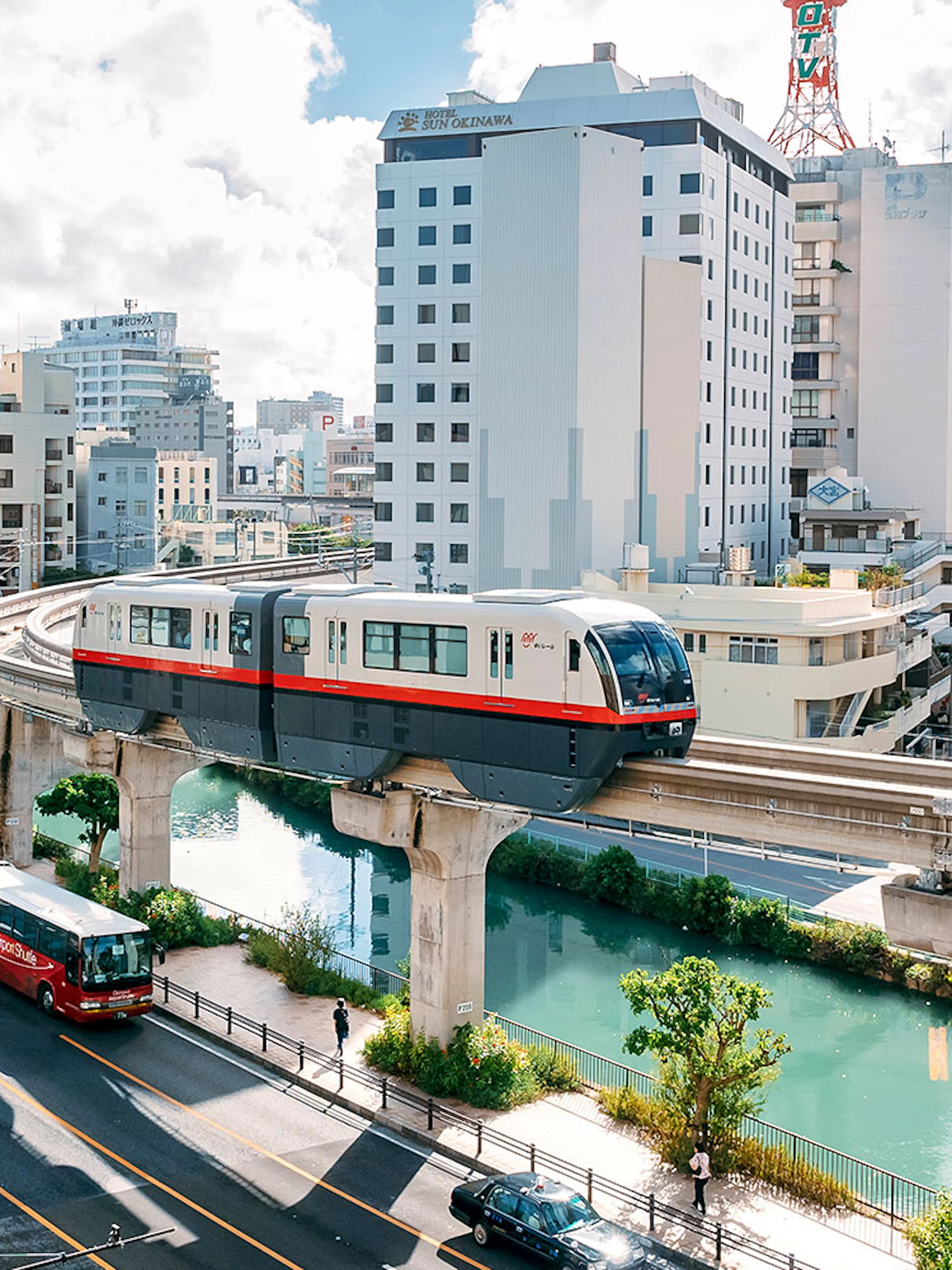 Okinawa Monorail passing through urban landscape with buildings and river below.