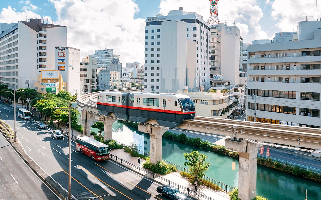 Okinawa Monorail passing through urban landscape with buildings and river below.