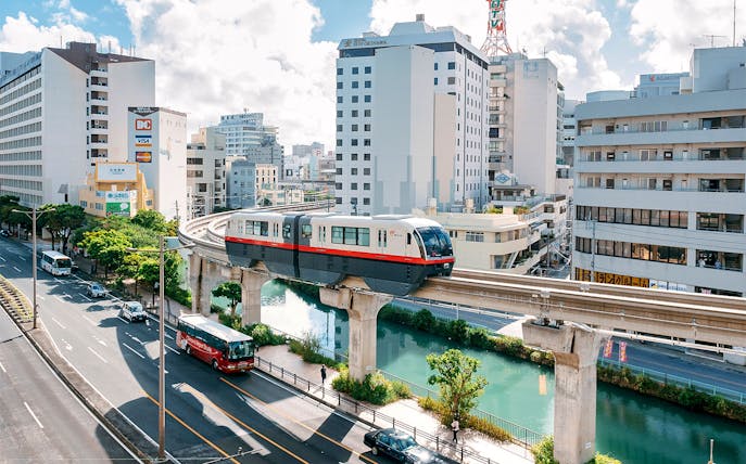 Okinawa Monorail passing through urban landscape with buildings and river below.
