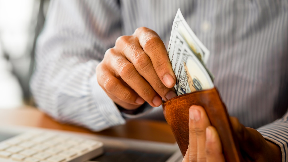 Hands placing cash into a wallet near a calculator.