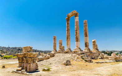 Temple of Hercules ruins at Amman Citadel, Jordan, with cityscape in the background.
