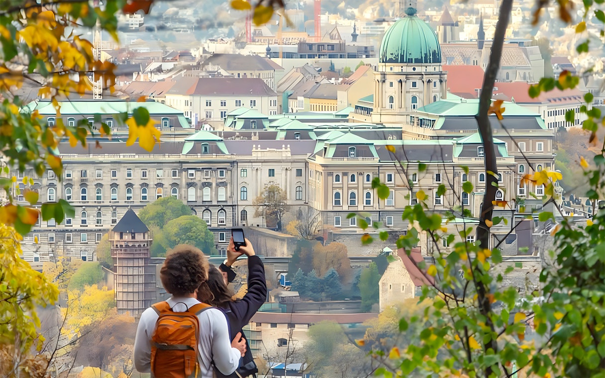 Tourists photographing Buda Castle in Budapest through autumn foliage.