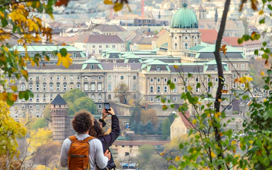 Tourists photographing Buda Castle in Budapest through autumn foliage.