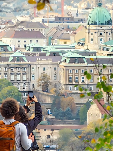 Tourists photographing Buda Castle in Budapest through autumn foliage.