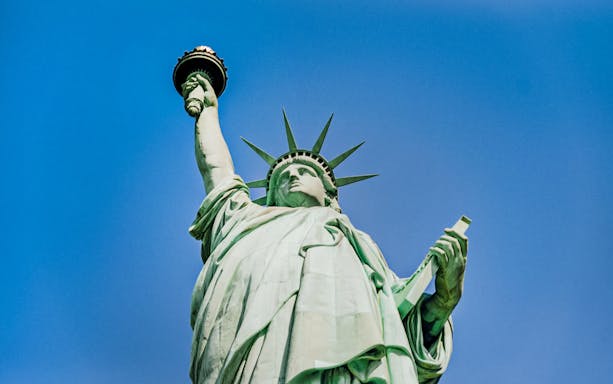Statue of Liberty holding torch against blue sky, New York City.
