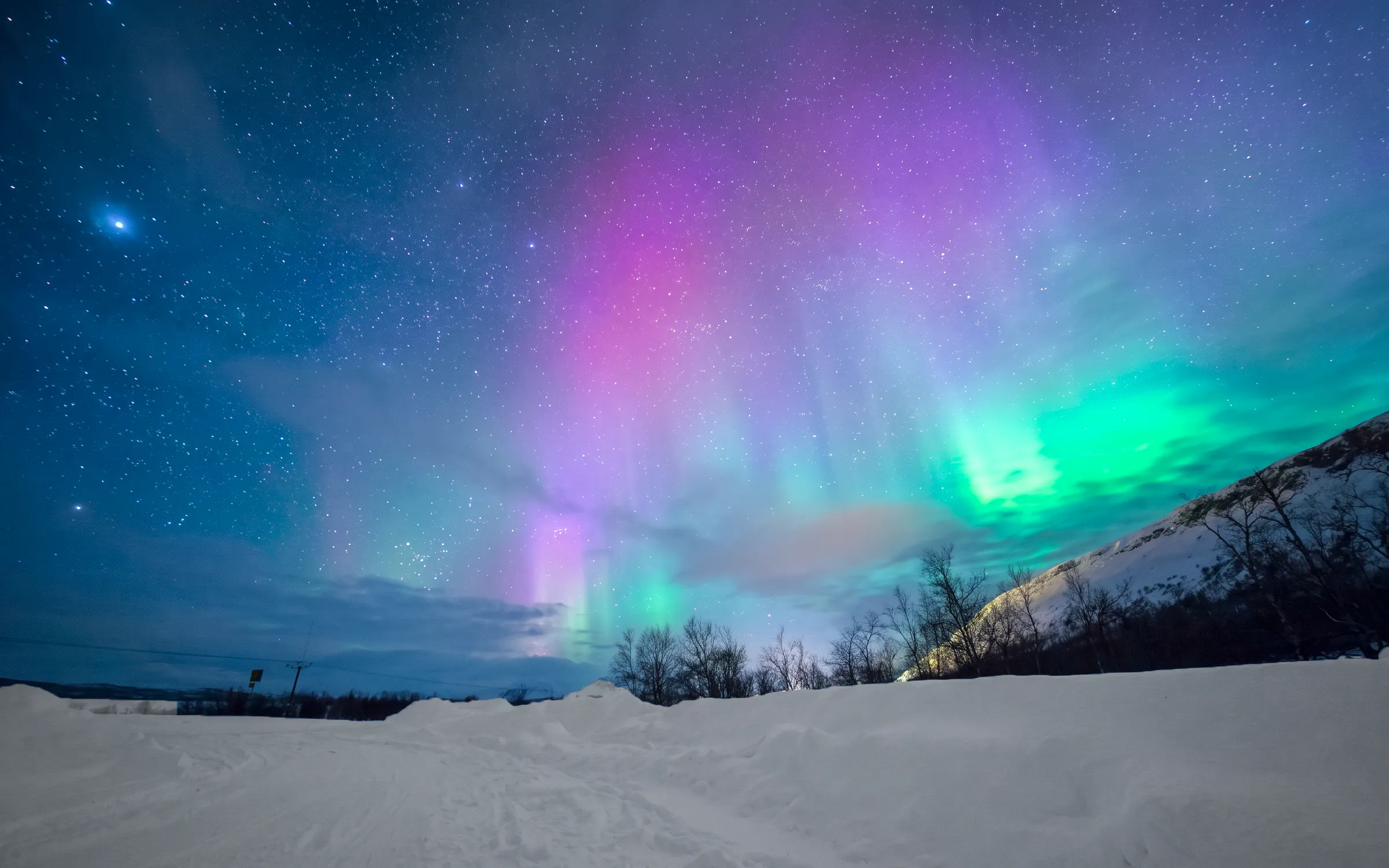 Northern lights over snowy landscape in Rovaniemi with starry sky.