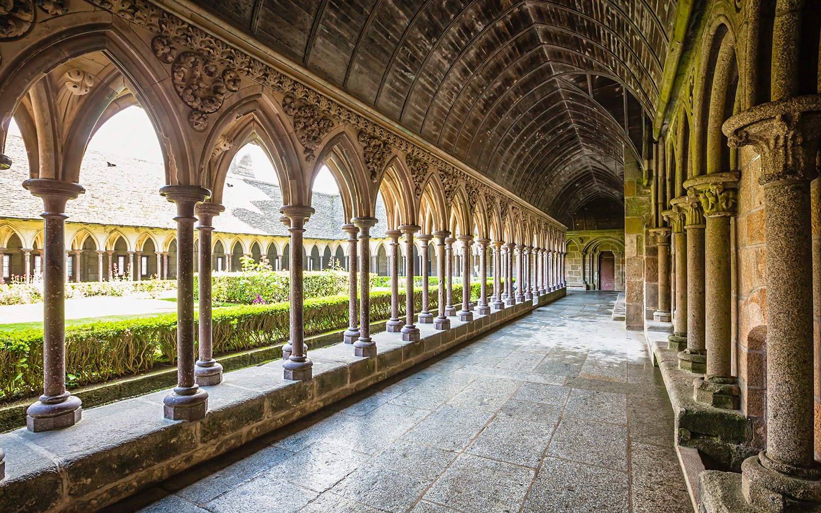 Cloister arches at Mont Saint-Michel, France, with garden view.