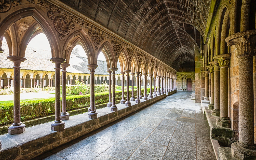 Cloister arches at Mont Saint-Michel, France, with garden view.