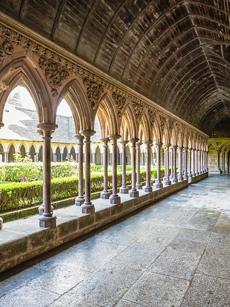 Cloister arches at Mont Saint-Michel, France, with garden view.