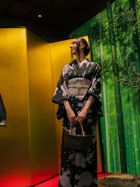 Tourist in kimono posing in front of bamboo-themed studio backdrop.