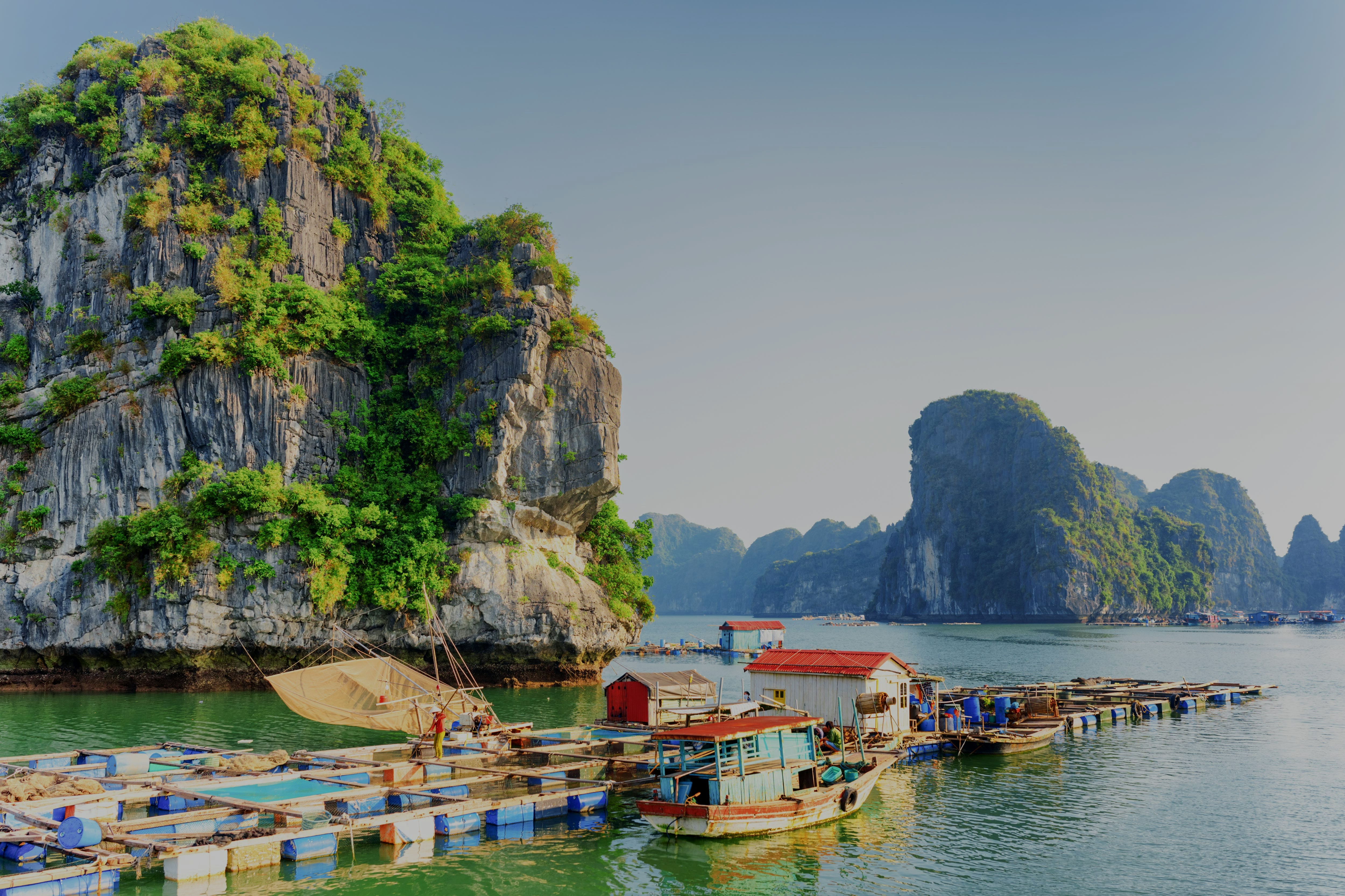 Floating fishing village with boats and limestone cliffs in the background.