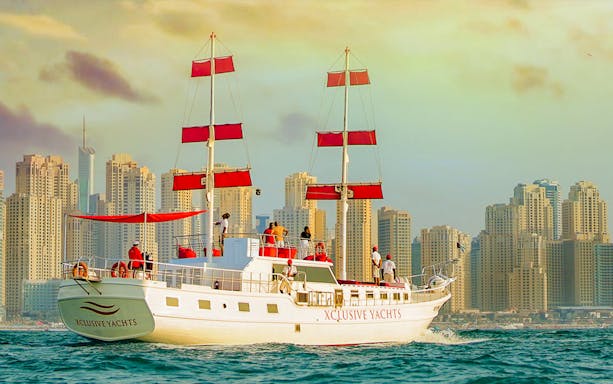 Sailing yacht with red sails in Dubai Marina against skyscrapers.