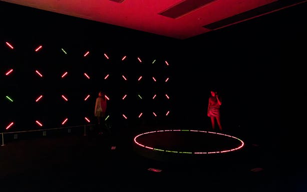 Visitors exploring Miyajimas Opposite Circle light installation in a dark room.