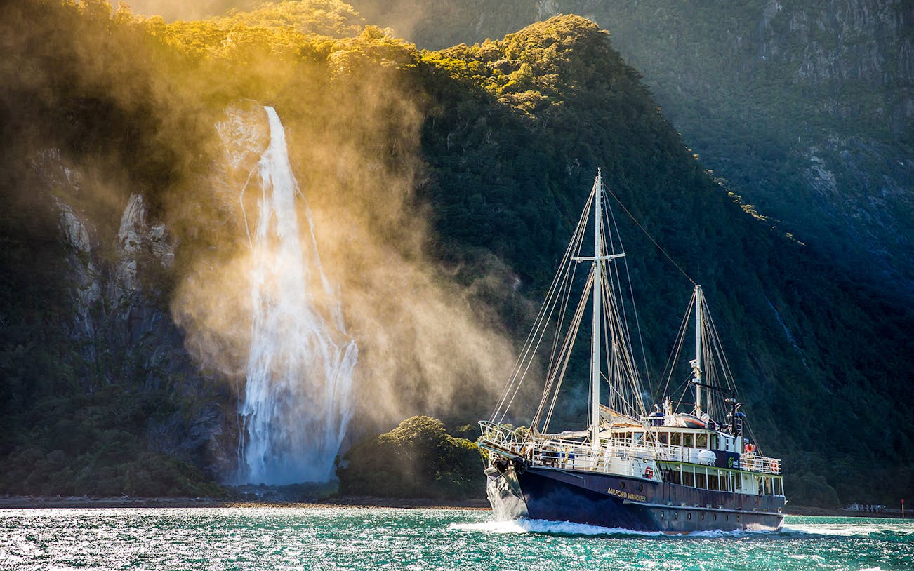 Cruise ship sailing near a waterfall in Milford Sound, New Zealand.
