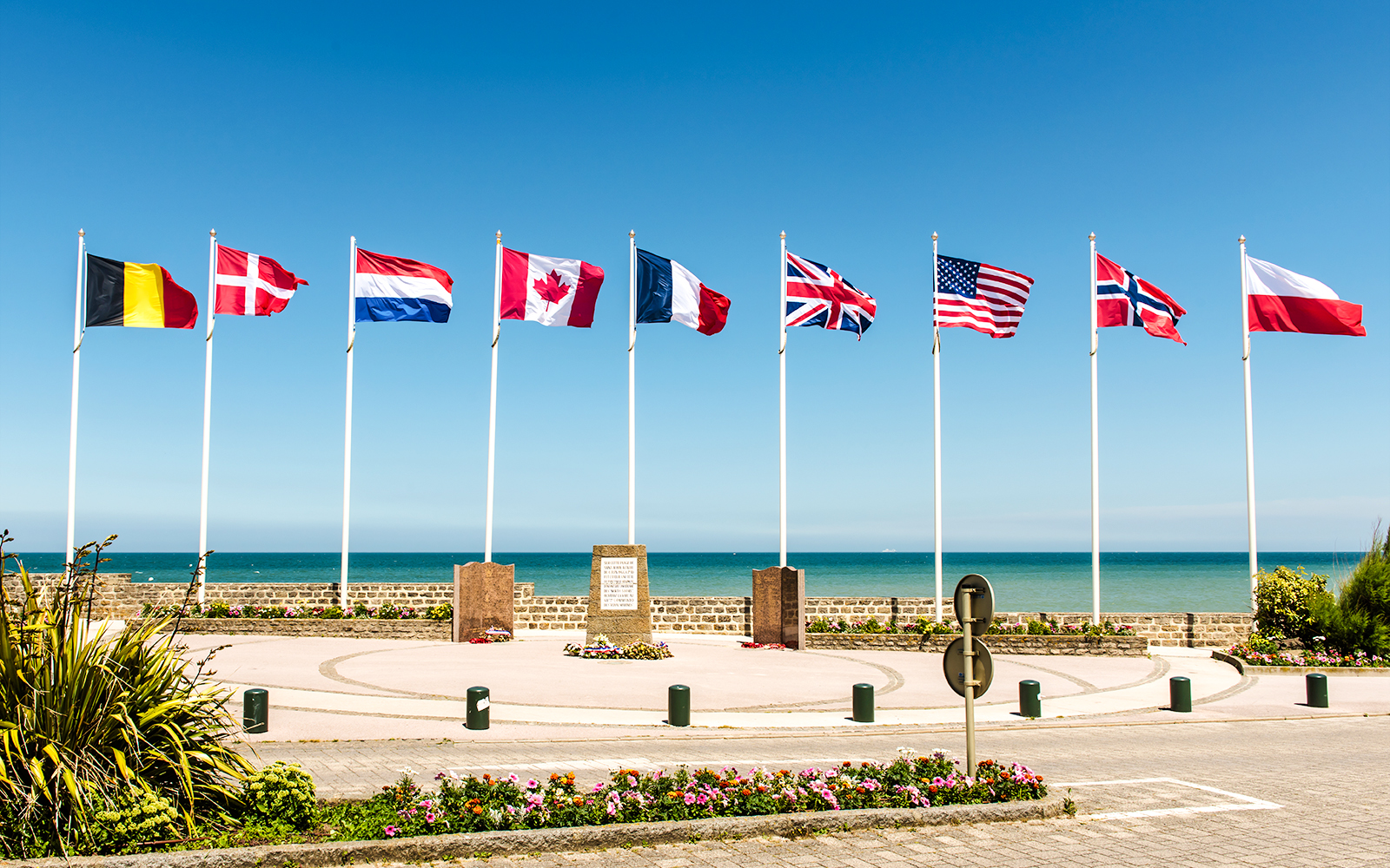 Flags at Juno Beach Monument in Normandy, France, with ocean backdrop.