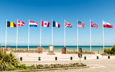 Flags at Juno Beach Monument in Normandy, France, with ocean backdrop.