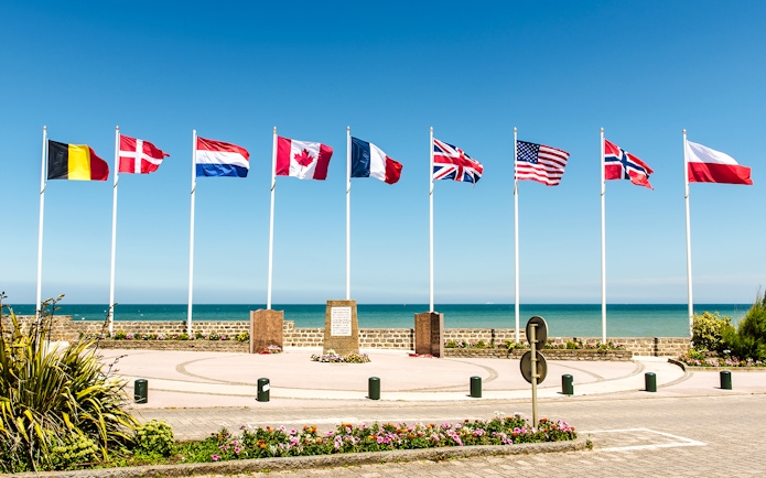 Flags at Juno Beach Monument in Normandy, France, with ocean backdrop.