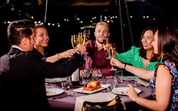 Guests toasting with champagne on a Seine River dinner cruise at night.