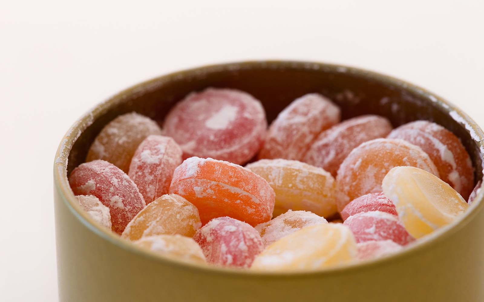 Different flavours hard drop candies in a tin box against white background.