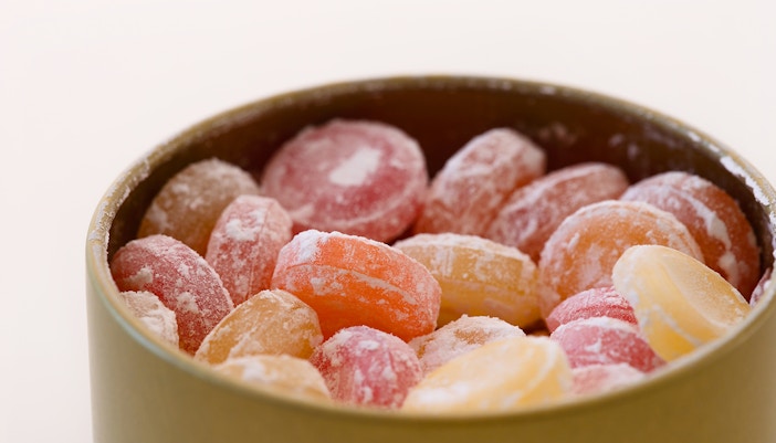 Different flavours hard drop candies in a tin box against white background.