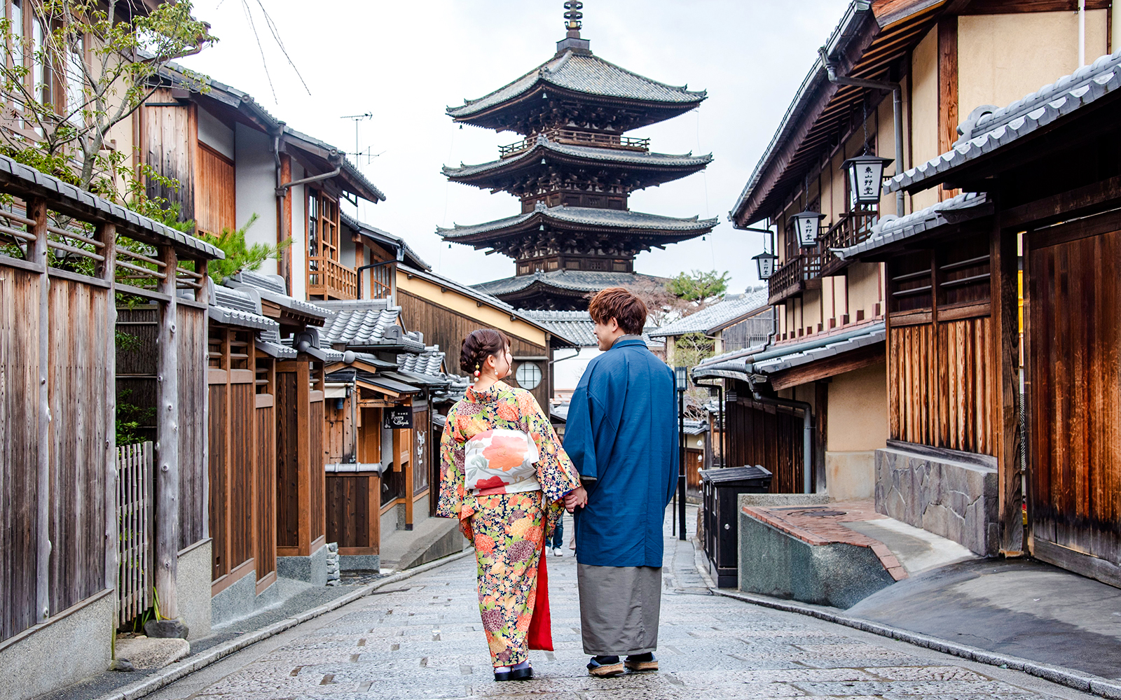 Couple in kimonos walking down a Kyoto street with a pagoda in the background.