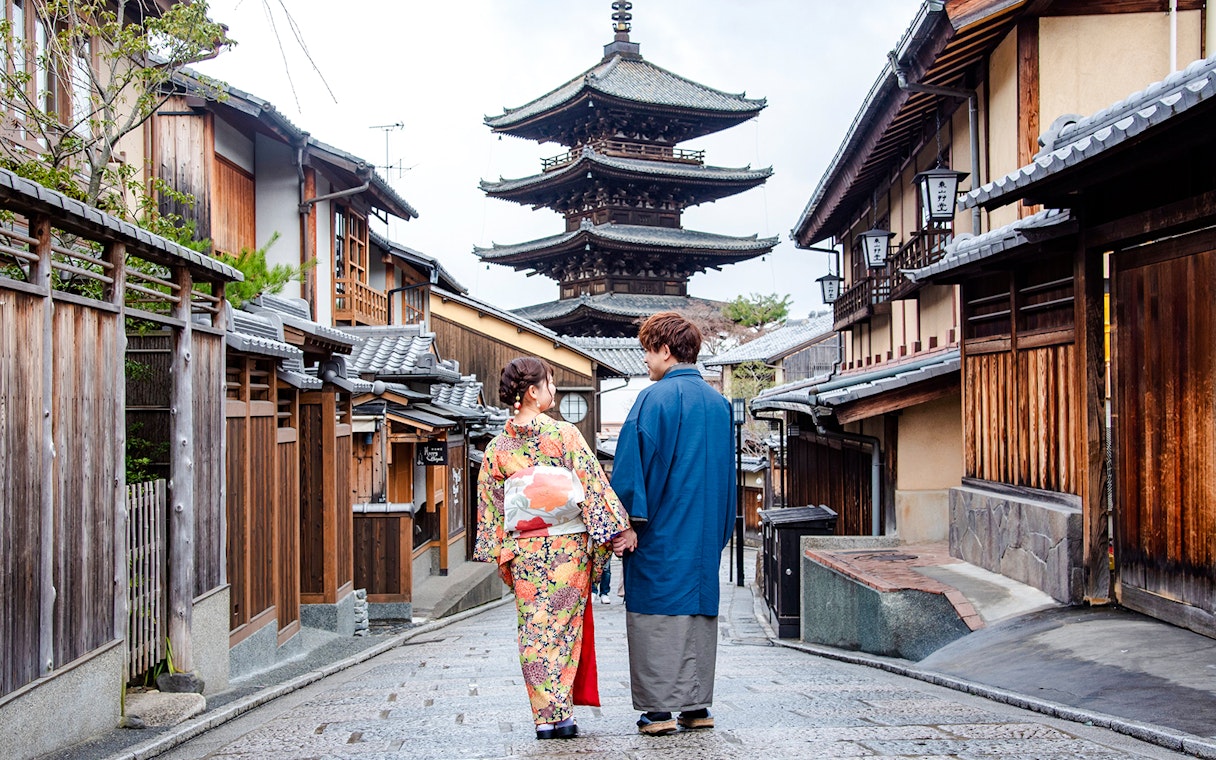 Couple in kimonos walking down a Kyoto street with a pagoda in the background.