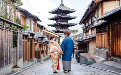 Couple in kimonos walking down a Kyoto street with a pagoda in the background.