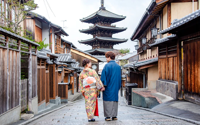 Couple in kimonos walking down a Kyoto street with a pagoda in the background.