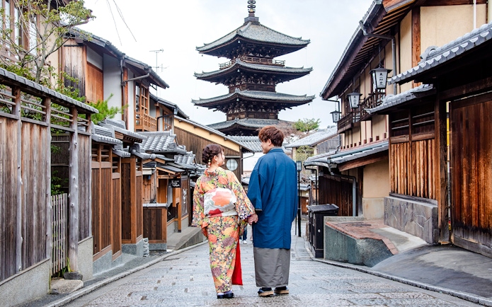 Couple in kimonos walking down a Kyoto street with a pagoda in the background.