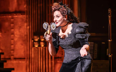 Performer on stage during Hadestown show, West End, holding a vintage microphone.