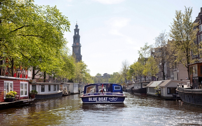 Blue boat cruising Amsterdam canal with Westerkerk tower in view.